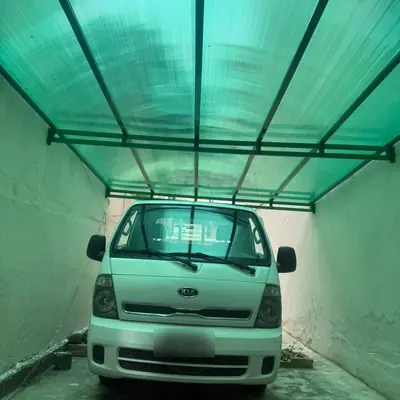 Cobertura de policarbonato verde sobre garagem com carro estacionado